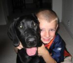A boy hugging his black Labrador Retriever